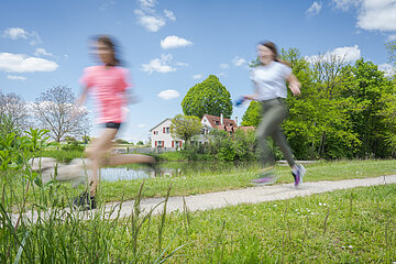 Zwei Mädchen rennen auf dem Weg neben dem Karlsgraben hintereinander. Die Mädchen sind leicht verschwommen.
