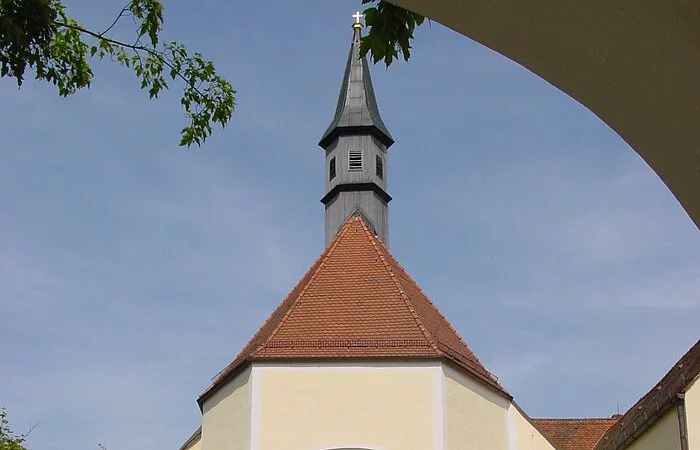 Blich durch den Torbogen auf die Franziskanerkirche mit geöffneter Kirchentür und dem Kirchenvorplatz im Vordergrund.