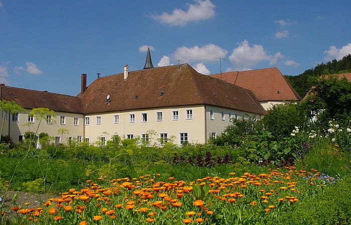 Blumen und Sträucher des Klostergartens, im Hintergrund Klostergebäude.