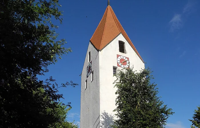 Großer Kirchturm umrahmt von hohen Bäumen.
