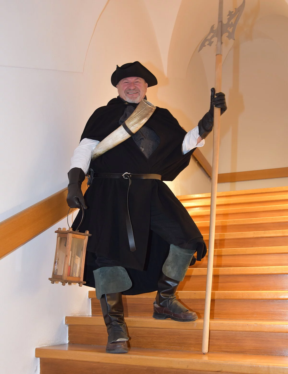 Nachtwächter Rudi Wittmann in Kluft mit Hellebarde und Laterne steht auf der Treppe im Gewölbe des Treppenhauses der Dom Augusto - Stiftung