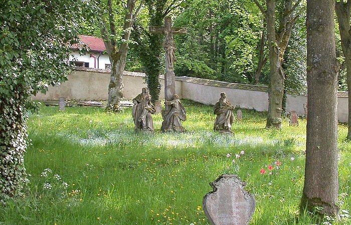 im Vordergrund ein Grabstein, im Hintergrund die barocke Kreuzigungsgruppe