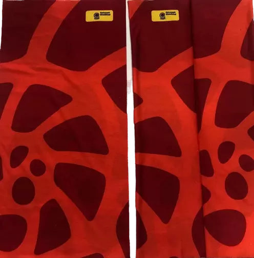 Zwei rote Schlauchschals nebeneinander, der Länge nach im Bild. Der rechte Schal hat eine Falte, welche den aufgedruckten Ammoniten verzerrt. Die Marke des Naturparks ist auf beiden Schals sichtbar.