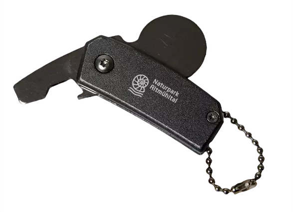 Schlüsselanhänger mit teilweise asugeklappten Einkaufswagenchip oben und teilweise ausgeklappten Flaschenöffner links. Zentral die Marke des Naturparks in weiß auf dem Korpus des Schlüsselanhängers