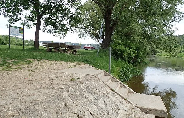 Der Bootseinstieg bestehend aus Stufen und glatter Fläche um die Boote hoch zu ziehen,  ist komplett aus Stein und Beton gebaut worden. Dahinter kann man die Infotafel für die Bootswanderer und die Sitzgelegenheit am Ufer sehen.