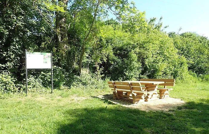 Eine Sitzgarnitur aus Holz auf dem Bootsrastplatz und dahinter steht eine Infotafel zum Bootwandern. Umgeben ist der Platz von Bäumen und Büschen.