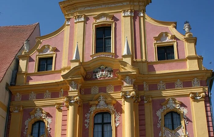 Die Staatliche Provinzialbibliothek von außen fotografiert. Das Gebäude im Frührokokobaustil  mit seiner reichen Fassadengliederung in rosa und gelber Farbe gehalten.