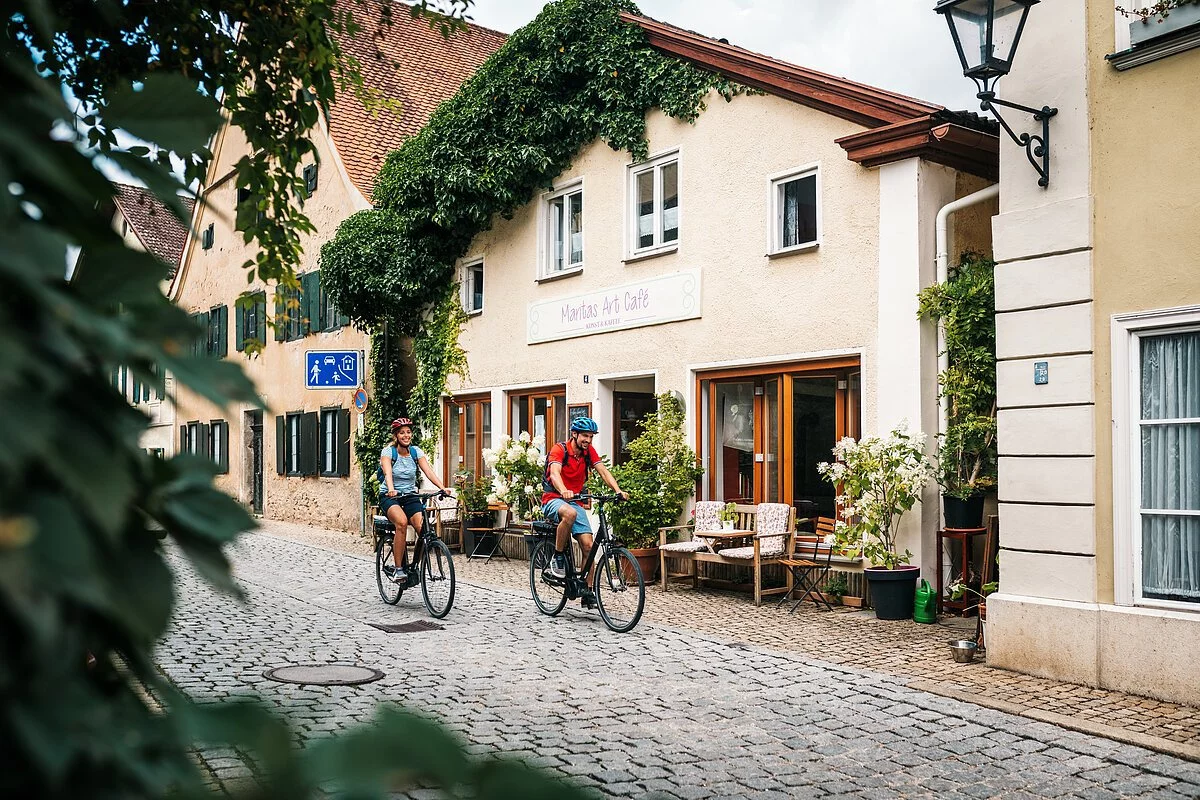 Zwei Radler mit blauem und rotem Shirt fahren durch die Altstadt Pappenheims.