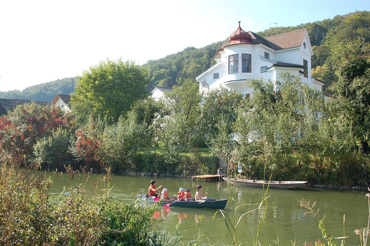 Schloss Inching von außen Eine Familie rudert auf der Altmühl am Schloss Inching vorbei. Das Schloss wird als Ferienhaus vermietet und trohnt inmitten von grünen Bäumen am Ufer.