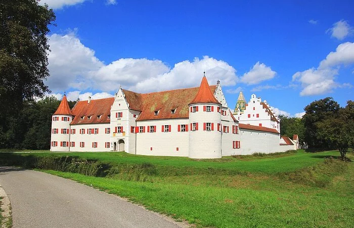 Das Schloss mit seinen roten Fensterläden und roten Dächern inmitten grüner Wiesen.
