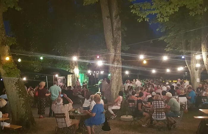 Biergartenbetrieb, Abendstimmung an der Stadthalle unter altem Baumbestand.
