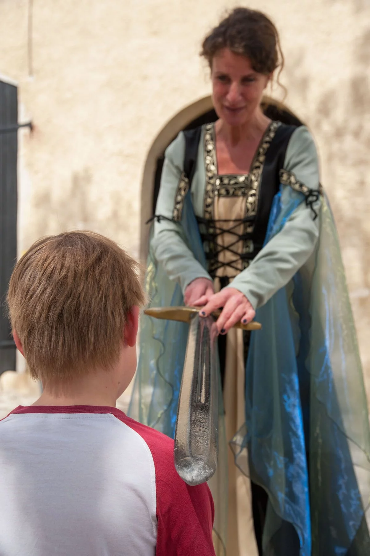 Die Schlossherrin in Gewand macht einen Ritterschlag bei einem Jungen