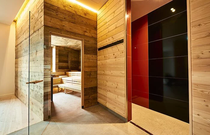 Die Glastür der Sauna aus Holz steht offen und wir können einen Blick auf die leeren Bänke darin werfen.