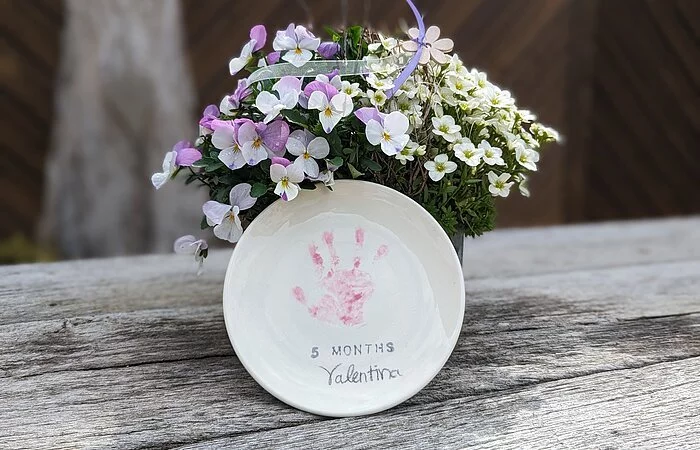 Ein Keramikteller schön vor einer Blumenvase dekoriert stehen auf einem Holztisch.