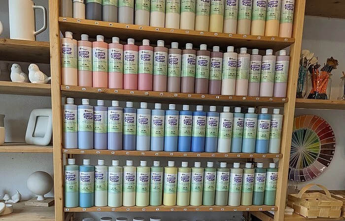 In einem Regel sind viele Keramikfarben und Rohlinge zu sehen, die den Teilnehmern zur Verfügung stehen.