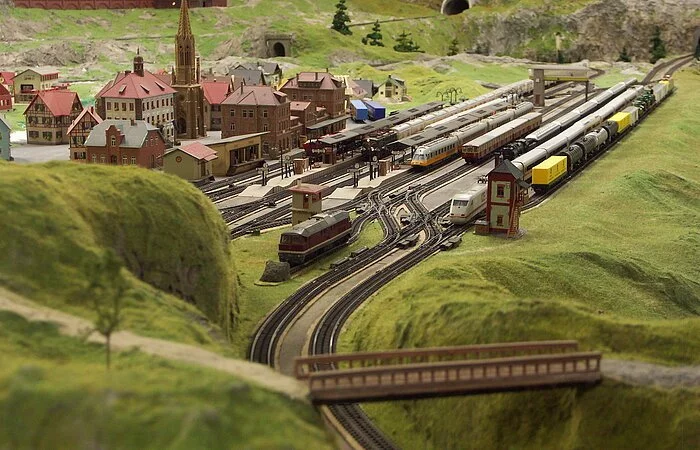Eine Miniaturlandschaft umgeben von grün. Eisenbahnschienen und ein Dorf.