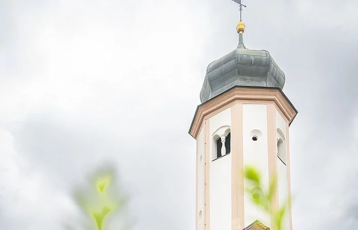 Seitenansicht der Lambertuskirche aus der Froschperspektive und bewölktem Himmel. Im Vordergrund befinden sich grüne Pflanzen.