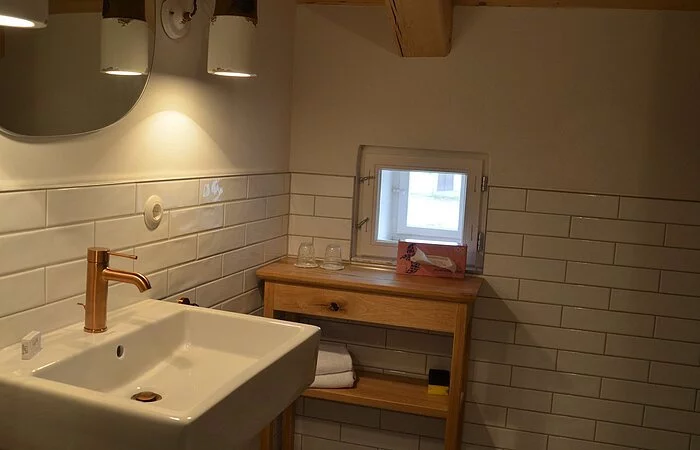 Eine Badezimmer der Gasthof Krone Kinding mit Waschbecken im Vordergrund und im Hintergrund ein Beistelltisch mit Spiegel