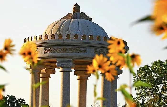 Fokus auf einen runden Steinpavillion im Schlosspark Dennenlohe. im Vordergrund gelbe Blumen.