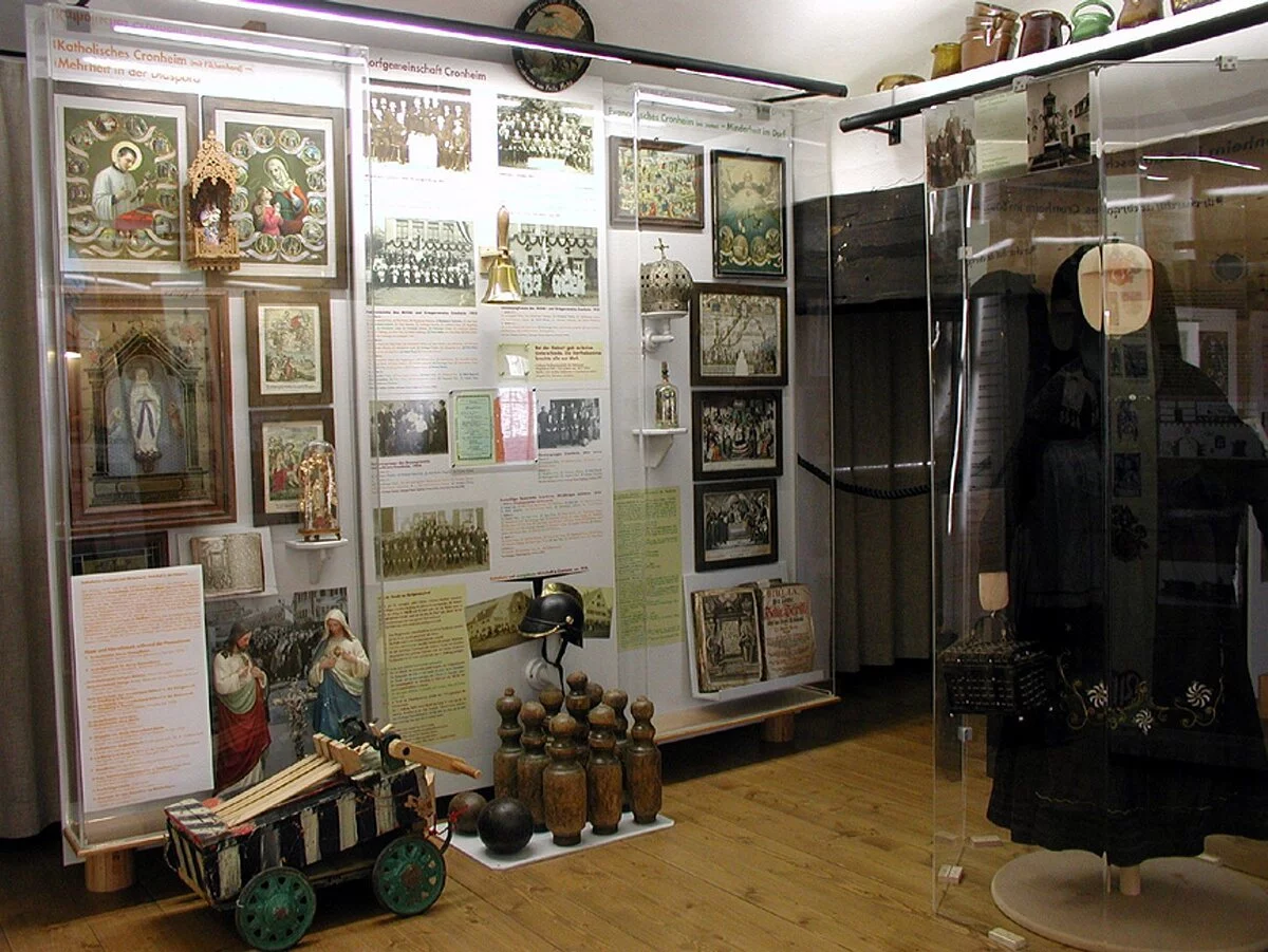 Eine Museumsausstellung mit einer alten schwarzen Tracht. Links daneben hängen christliche Bilder und beschreibende Texte an den Wänden.