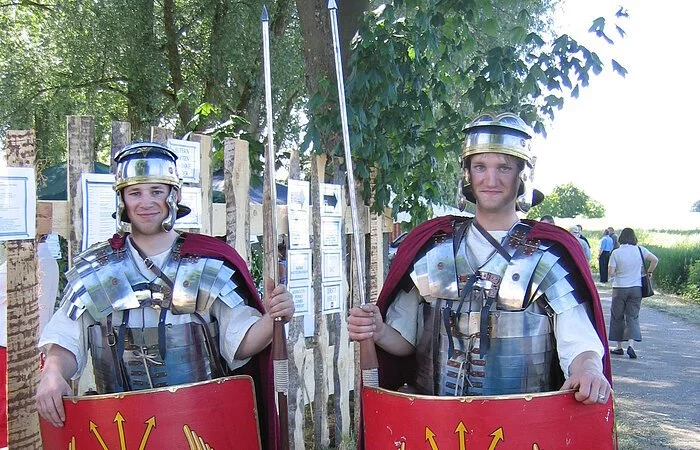 Zwei Männer verkleidet als römische Legionäre. Sie trage eine metallenen Brustpanzer und Helm. Eine Lanze und ein rotes Schutzschild.