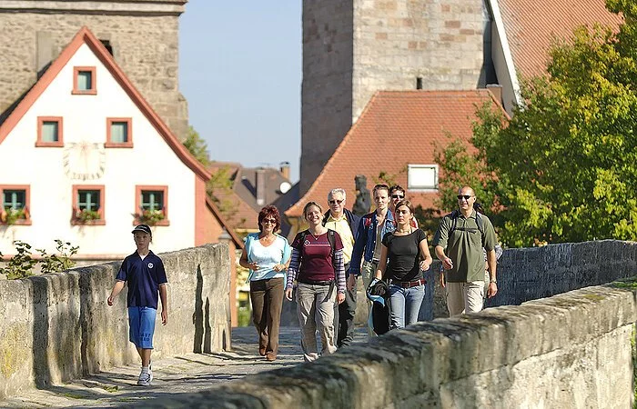 Wanderer auf der steinernen Altmühlbrücke bei Ornbau. Im Hintergrund die Häuser der Stadt Ornbau.