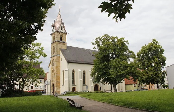 Blick auf die Pfarrkirche St. Sebastian, die teilweise hinter Bäumen verborgen ist.