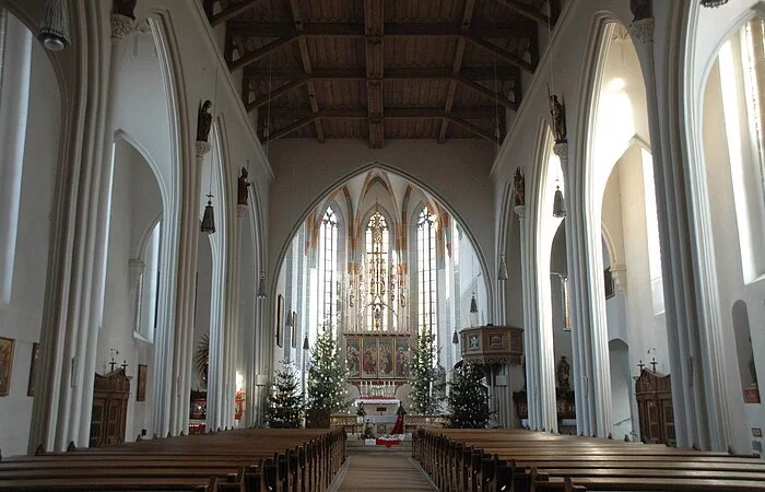 Blick in das lichtdurchflutete Innere mit dem Hauptaltar der von vier wegeschmückten Christbäumen umrahmt ist. Rechts vor dem Altar sieht man die Kanzel.