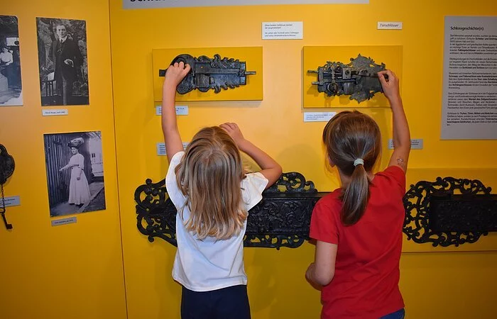 Zwei Kinder probieren alte, an der Wand befestigte Schlösser aus