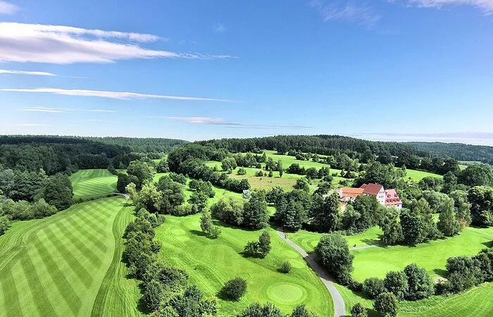 Luftaufnahme einer Golfanlage. Große grüne Wiesen. Dazwischen Bäume und Sträucher.