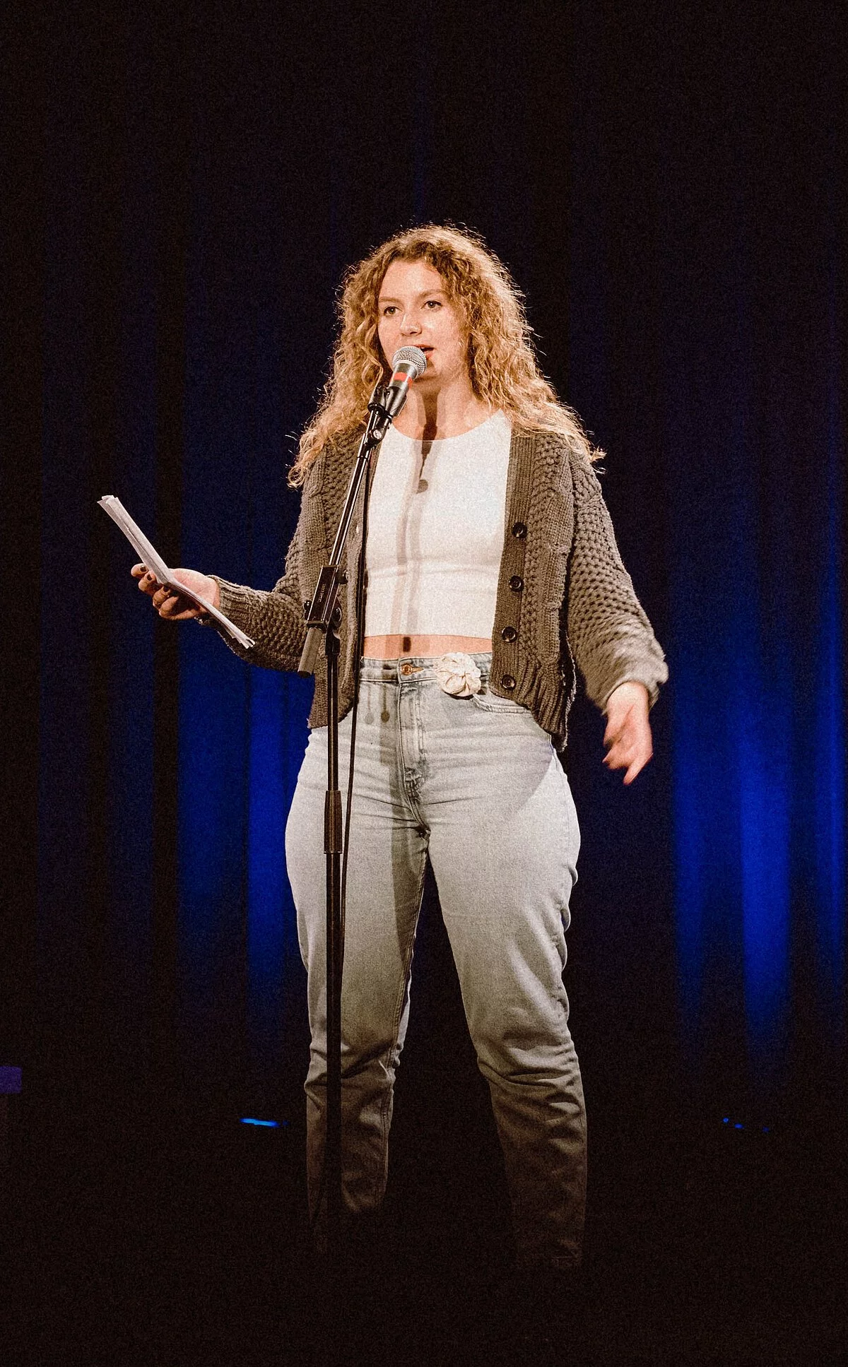 Junge Slammerin steht vor einem Mikrofon, in der rechten Hand hält sie Papier