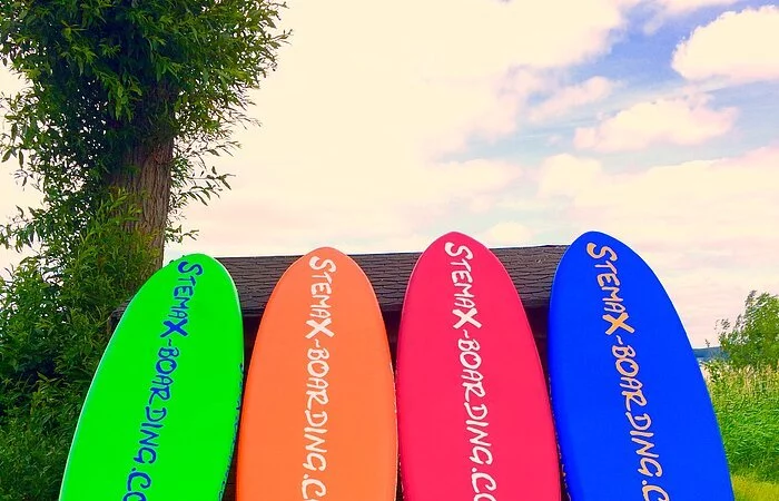 Grünes, orangenes, pinkes und blaues Board lehnen an einem Zaun.