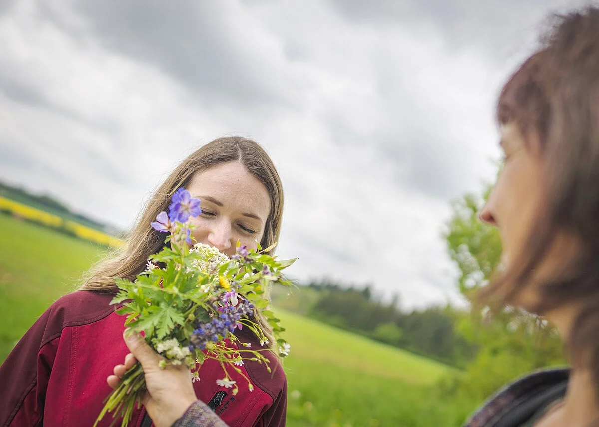 Teilnehmerin riecht an einem bunten Wiesenstrauß mit geschlossenen Augen.