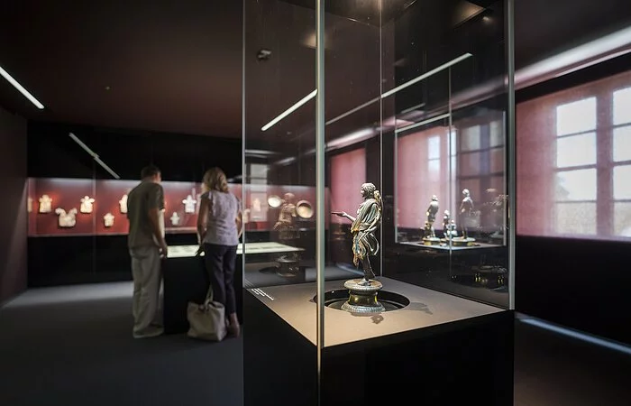 Im Vordergrund ist eine Glasvitrine mit einem römischen Exponat. Im Hintergrund schauen sich eine Frau und ein Mann die Exponate an.