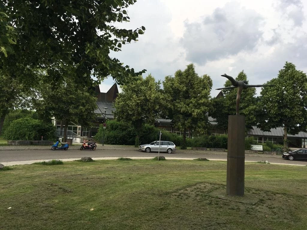 Das Bild zeigt eine Statue im Stauferpark darum sehr viel grün mit Sträuchern, Bäumen usw.