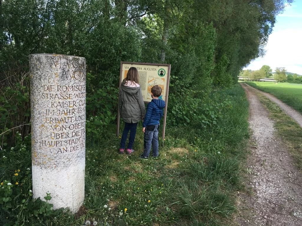 Meilenstein Via Claudia Augusta Blick von zwei Kindern auf die Informationstafel und daneben der Meilenstein der Römerstraße Via Claudia Augusta.