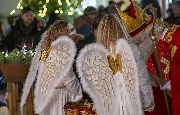 Zwei Mädchen mit Engels- und Mann im Nikolauskostüm beim Gabenverteilen