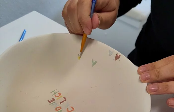 Ein Keramikteller wird mit bunten Farben und Buchstaben verziert.