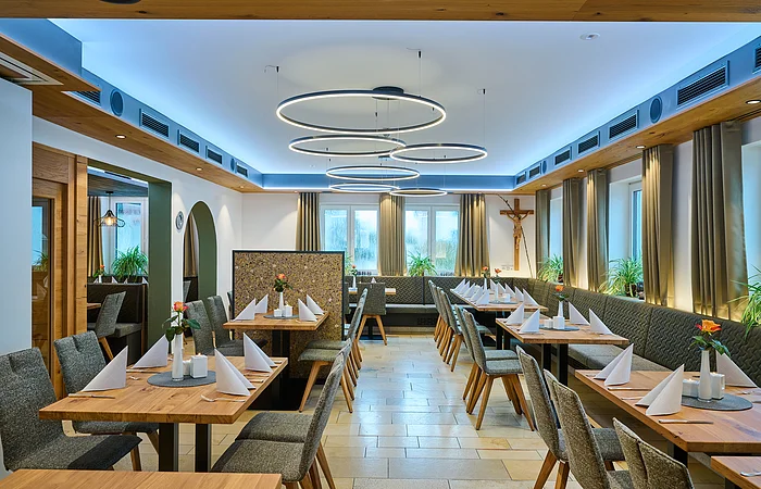 Der schmale längliche Raum ist links und rechts mit Tischen und Stühlen ausgestattet. Die Tische sind festlich gedeckt. Rechts kann man in den Garten durch die Fenster schauen.