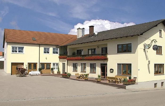 Der Landgasthof in L-Form ist hellgelb gestrichen. Der Balkon ist mit Geranien bestückt.