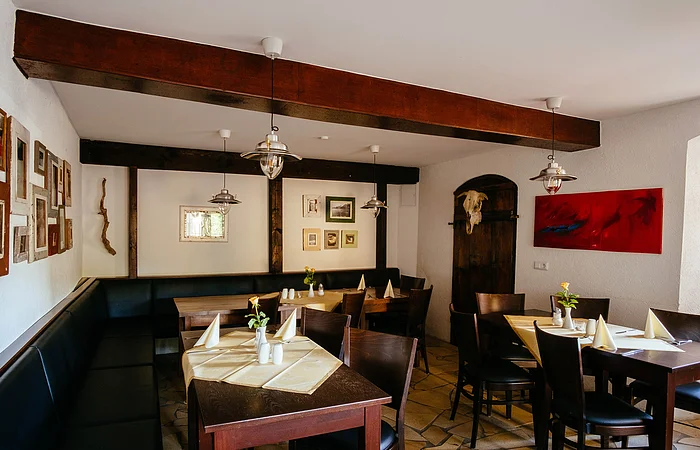 Die Einrichtung ist in dunklem Holz gehalten. Die Tische sind mit weißen Tischdecken und Servietten eingedeckt. Die weißen Wände sind mit Bildern dekoriert.