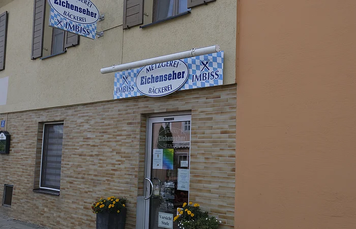 Die Eingangstür der Metzgerei mit dem Logo darüber ist zu sehen.