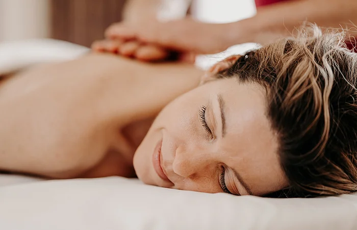 Eine Frau liegt auf dem Rücken auf einer Massageliege. Ihr Rücken wird von Händen massiert.