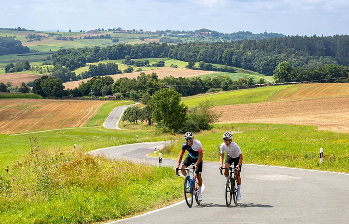 Zwei Radler treten im Wiegetritte einen kleinen Anstieg auf der Jurahochebene empor