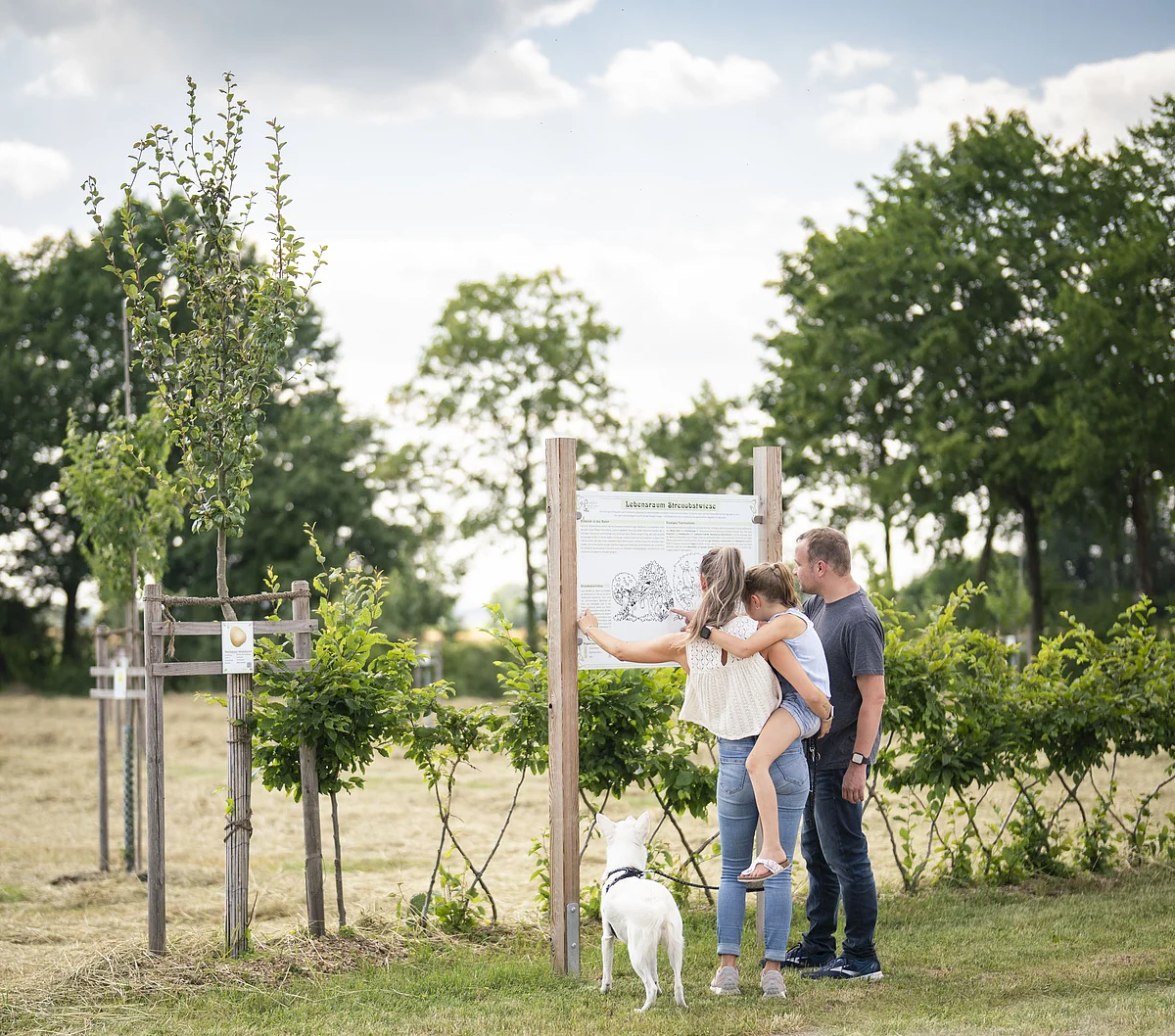 Eine Familie steht an einer Informationstafel im botanischen Obstlehrgarten.