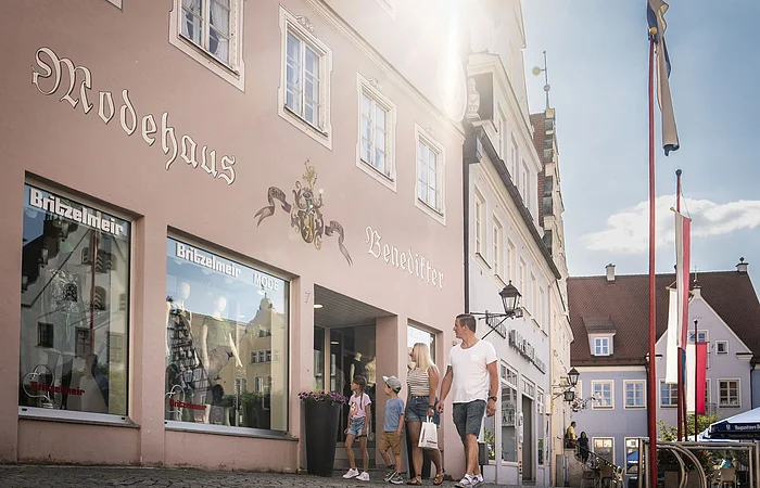 Eine Familie spaziert entlang dem Modehaus Britzelmeir am historischen Marktplatz.