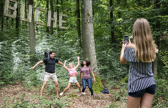 Eine Familie macht ein Foto mit einer Buche, einer Station im Walderlebnispfad.