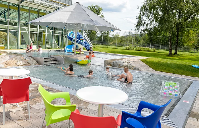 Außenbereich des Sport- und Freizeitbades Greding mit Planschbecken, Wasserrutsche und Sitzgelegenheiten