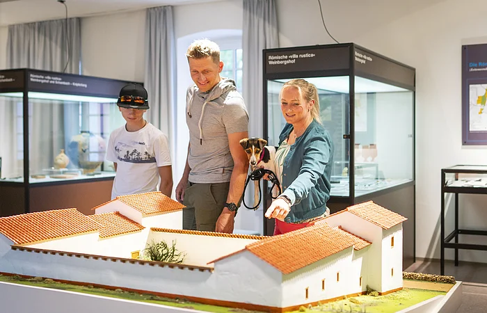Eine Familie besucht die Abteilung der Abteilung Vor- und Frühgeschichte im Museum. Sie Blicken auf eine Nachbildung einer sogenannten Villa Rustica.