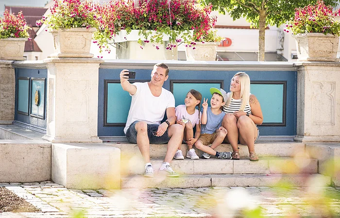 Familie macht ein Selfie am historischen Marktplatz. Im Hintergrund ist der Marienbrunnen zu sehen.